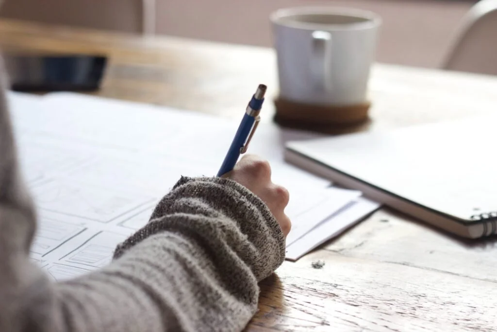 Ielts student taking notes during a lesson on paper with a cup of coffee