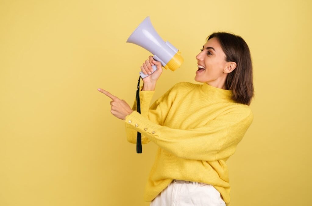 young-woman-yellow-warm-sweater-with-megaphone-speaker-screaming-left-pointing-index-finger